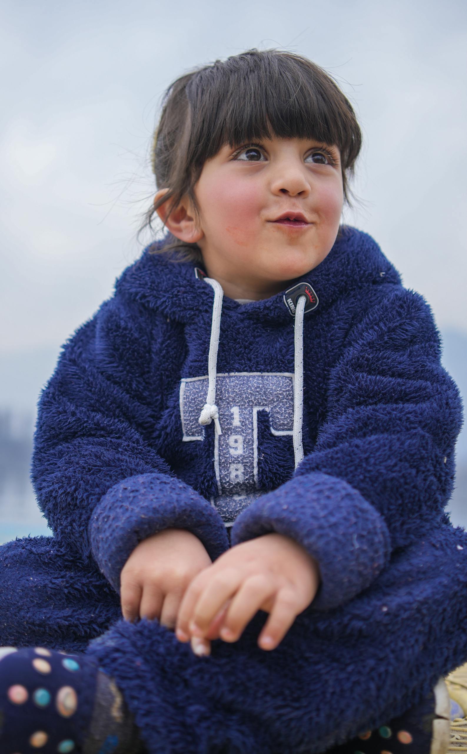 A little girl sitting on the ground wearing a blue hoodie