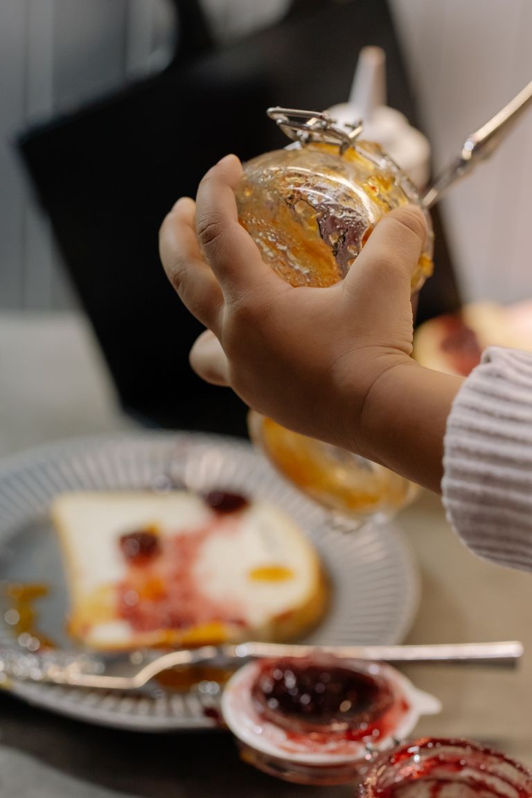 A child is seen spreading jam on a slice of toast, enhancing a delicious breakfast or snack scene.