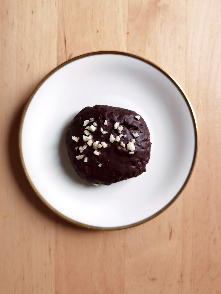 A chocolate-covered donut topped with almond pieces on a elegant white plate.