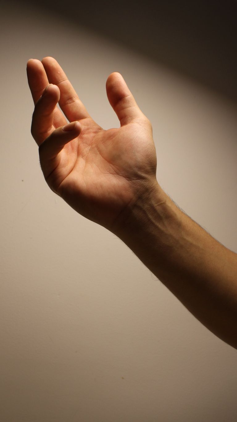 A close-up photo of an adult hand outstretched against dark to light gradient background