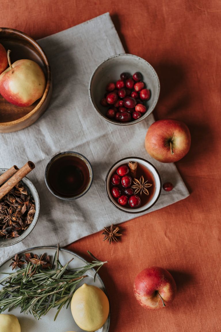 A warm, inviting flatlay of mulled wine ingredients including apples, cranberries, herbs, and spices on a rustic background.