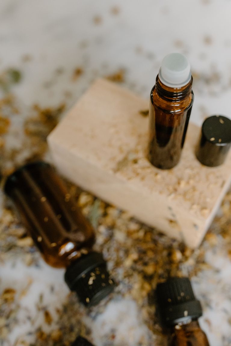 Brown glass roller bottles for essential oils on a wooden block surrounded by natural elements.