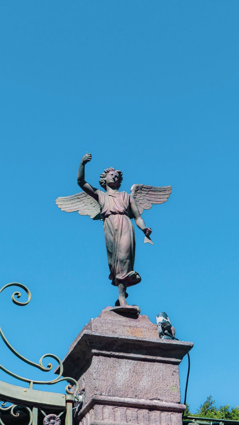 Elegant angel statue with outstretched wings atop a pedestal under a clear blue sky in Puebla, Mexico.