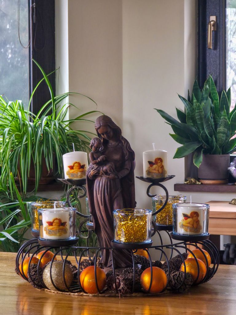 Indoor candle setup with religious statue and greenery.