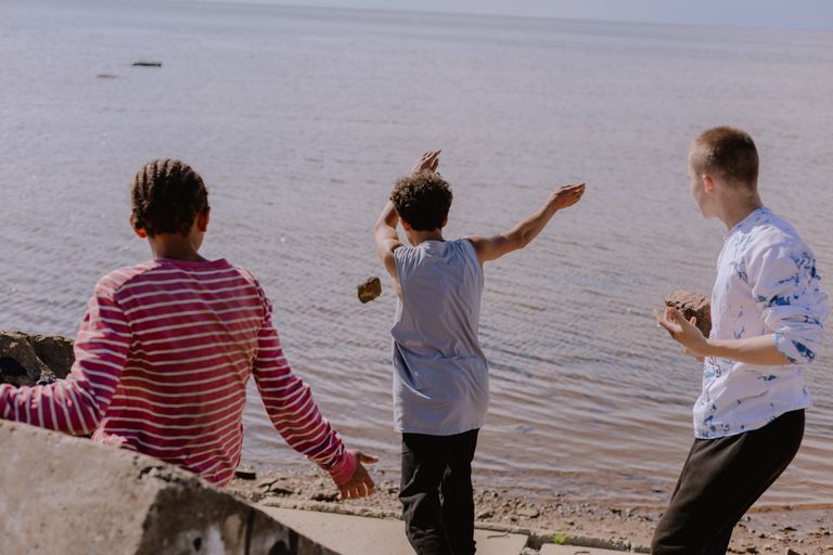 Three boys enjoying a carefree day by the river, joyfully skipping rocks together.