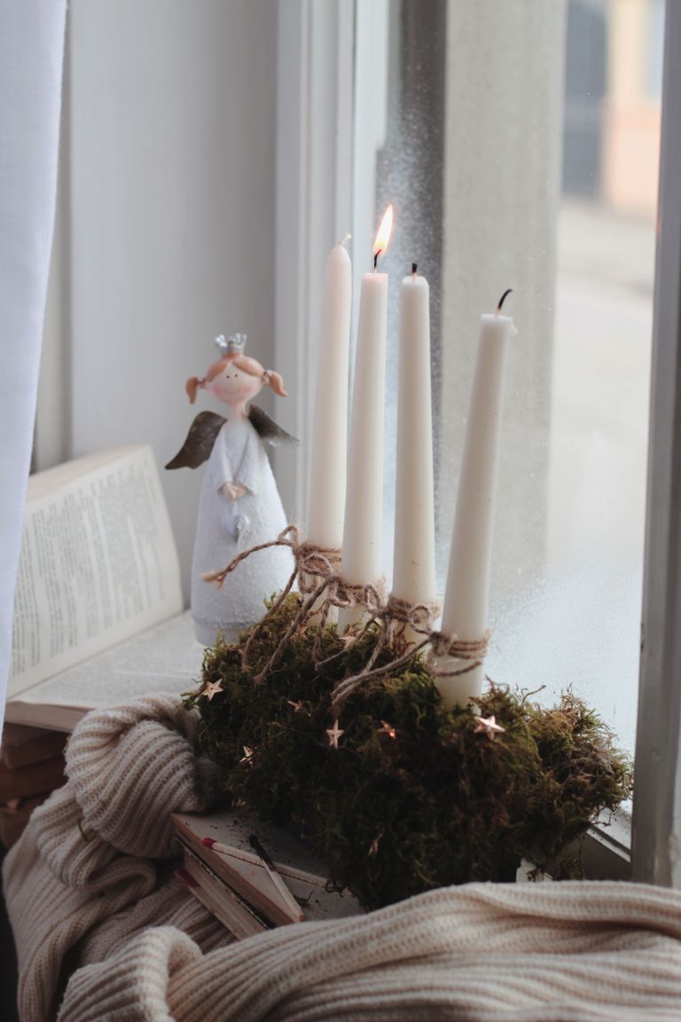 Warm intimate scene of white candles and angel figurine on a window sill.